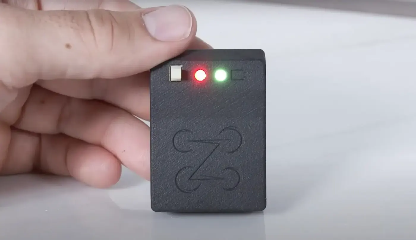 A small black Zing Remote ID module held between two fingers