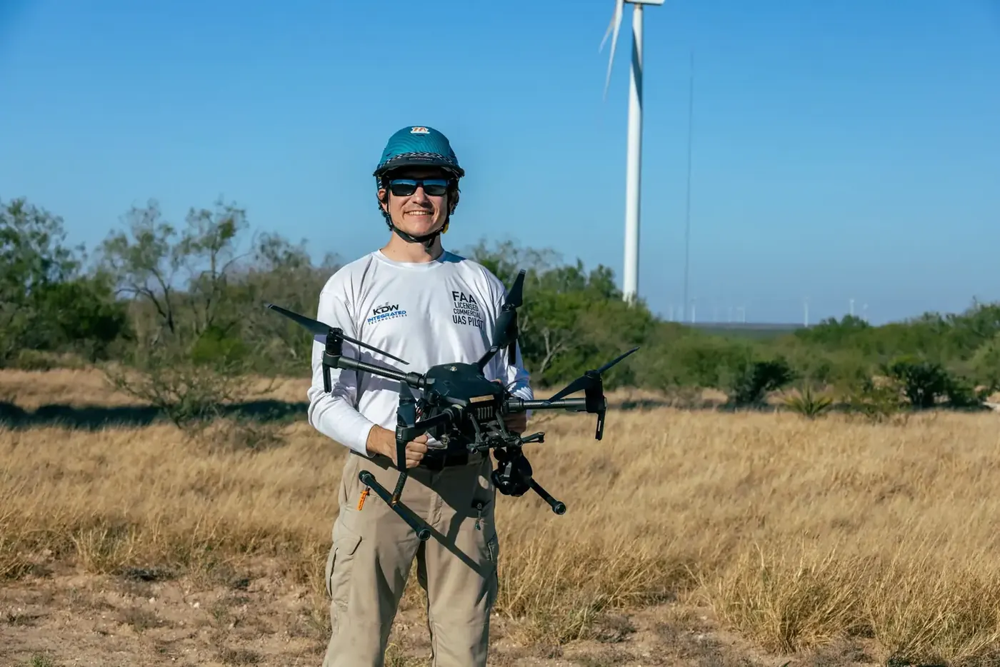 Pilot holding an enterprise drone in a field near wind turbines